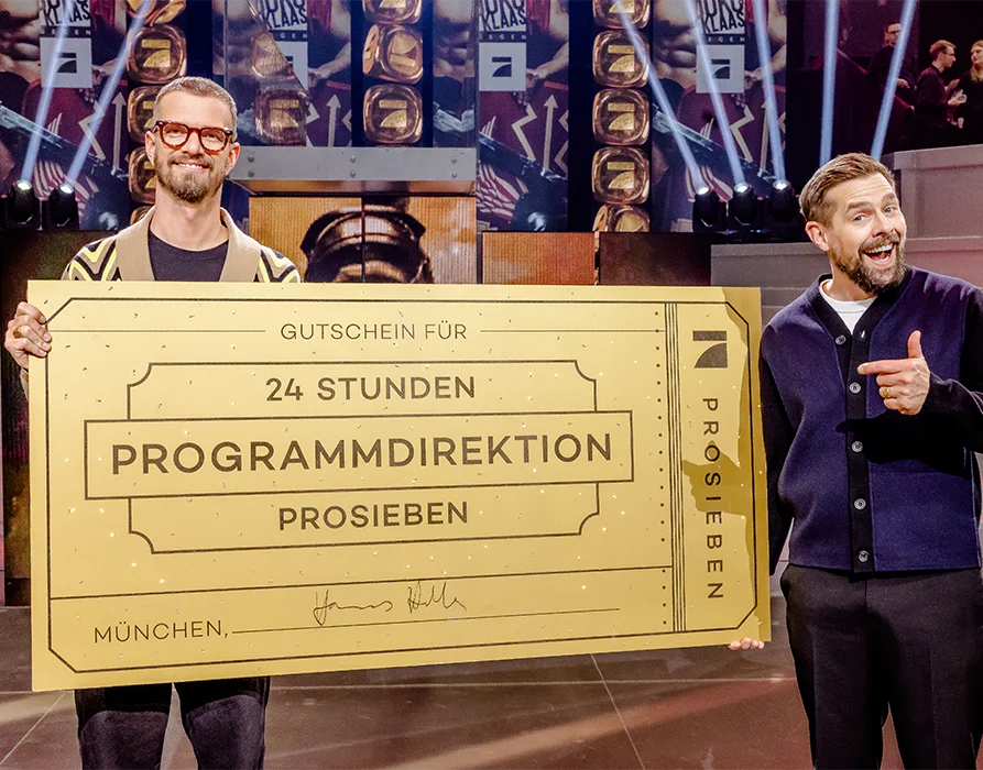 Joko and Klaas hold a large voucher with a German inscription saying ‘Voucher for 24 hours programme management ProSieben’ (Photo)