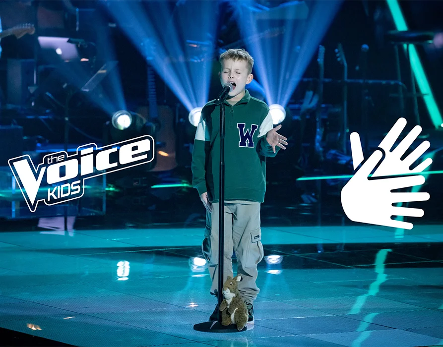 A boy sings into a microphone on a stage illuminated in blue-green light. A soft toy squirrel stands next to it. The ‘the Voice Kids’ logo is shown in the picture on the left. On the right there is a graphic of two hands. (Photo)