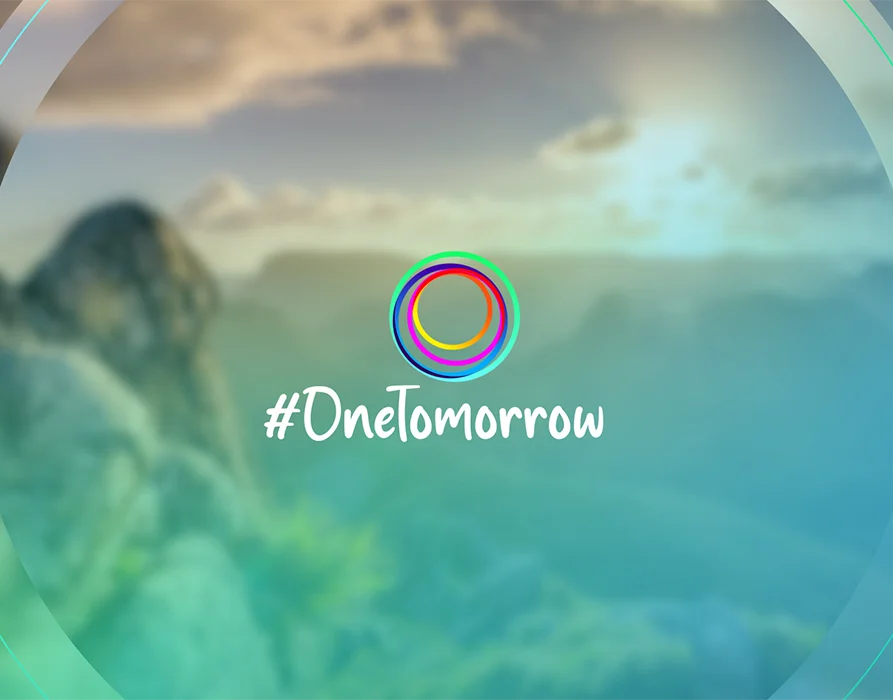 In the foreground: Logo consisting of the lettering #OneTomorrow and colourful circles. In the background: Blurred image of an alpine landscape with a sunset. (Photo)